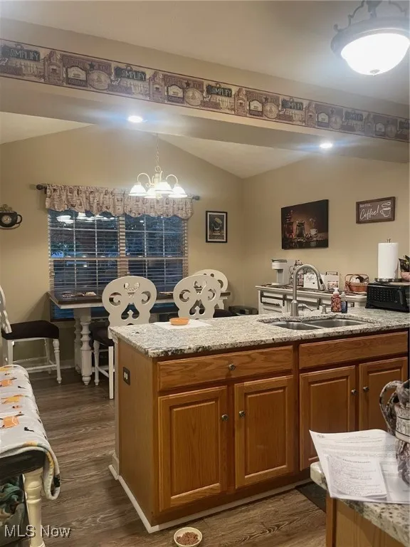 Kitchen featuring brown cabinetry, light stone counters, dark wood-style flooring, and a peninsula