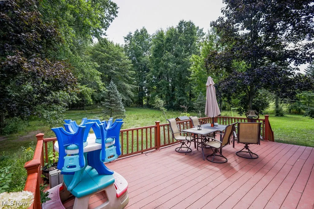 Deck with outdoor dining area, a yard, and view of scattered trees