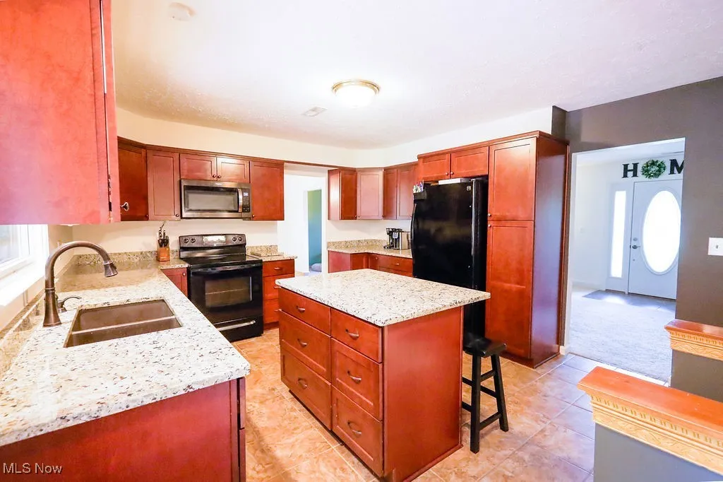Kitchen featuring black range with electric stovetop, a center island, a kitchen bar, stainless steel microwave, and light stone countertops