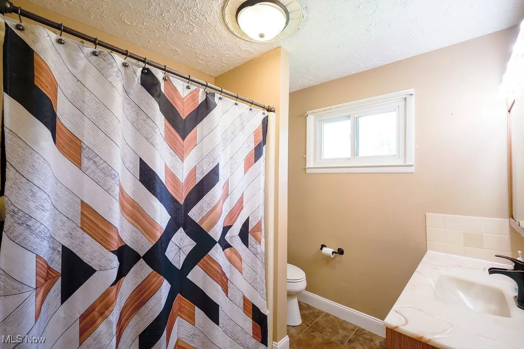 Bathroom featuring a textured ceiling, vanity, tile patterned flooring, and a shower with curtain