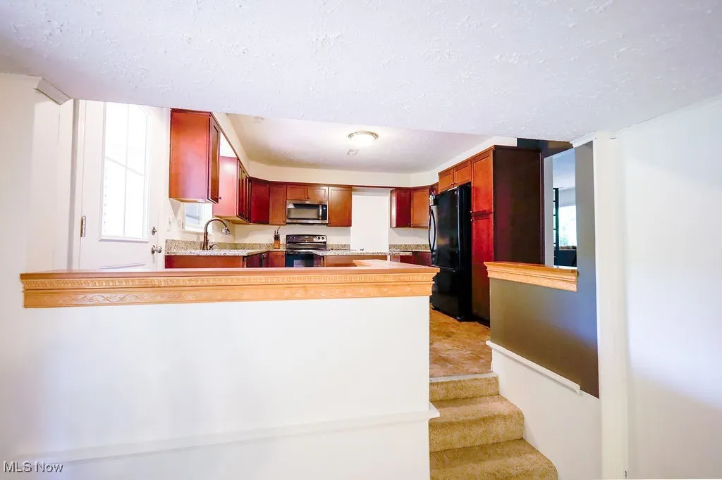 Kitchen with light countertops, a textured ceiling, black appliances, a peninsula, and dark brown cabinets