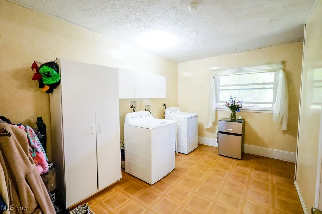 Laundry room with a textured ceiling, washing machine and dryer, cabinet space, and light floors
