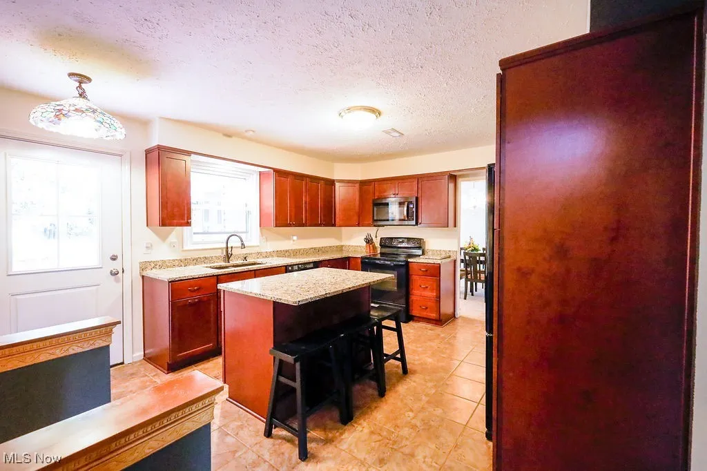 Kitchen featuring a kitchen bar, black appliances, a textured ceiling, light stone counters, and light tile patterned floors