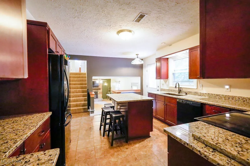 Kitchen featuring reddish brown cabinets, light stone countertops, a textured ceiling, and a kitchen island
