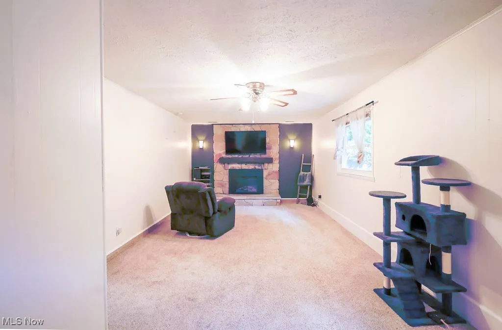Living area with a textured ceiling, carpet, a ceiling fan, and a stone fireplace