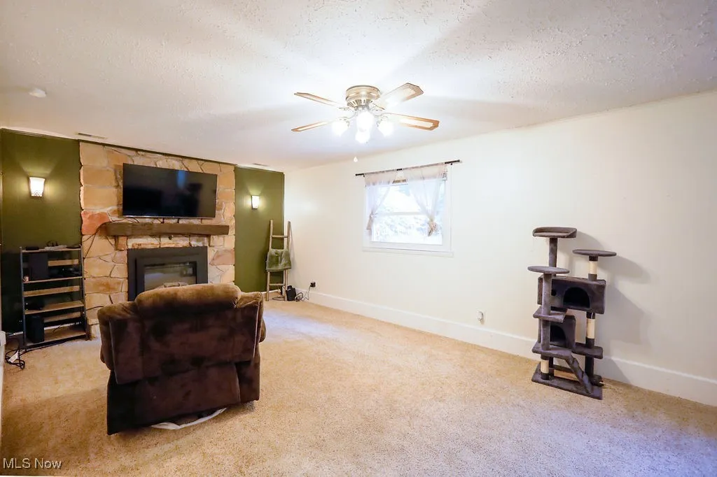 Sitting room with a textured ceiling, carpet floors, a stone fireplace, and ceiling fan