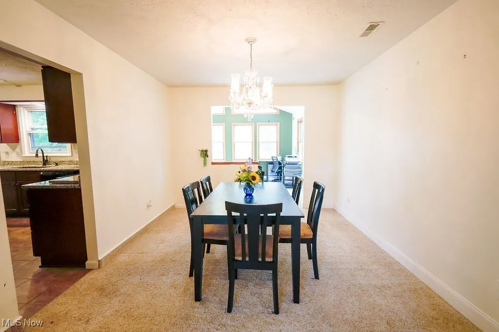 Dining space with light colored carpet, a chandelier, and a textured ceiling