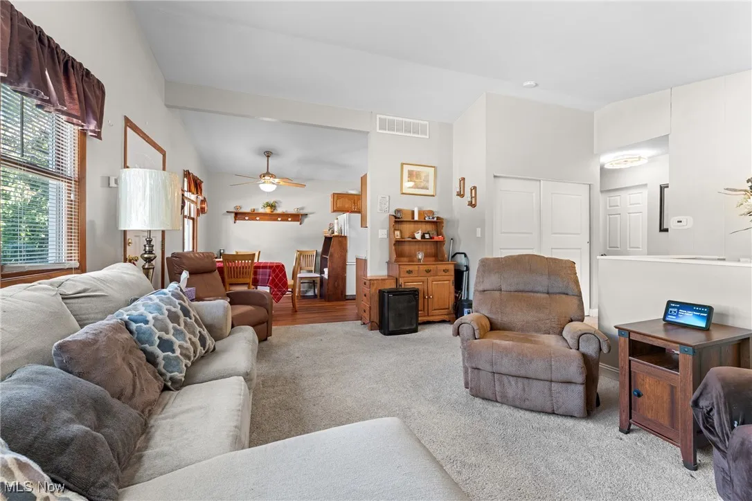 Living room with lofted ceiling, carpet flooring, and ceiling fan