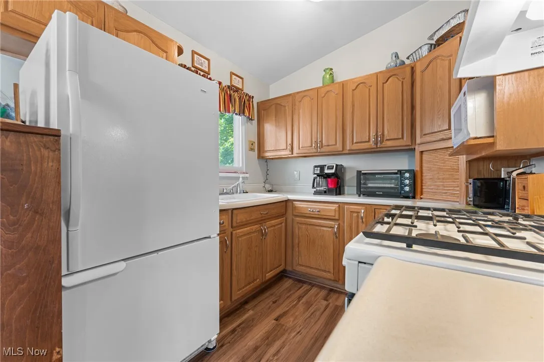 Kitchen with white appliances, lofted ceiling, brown cabinetry, custom exhaust hood, and light countertops