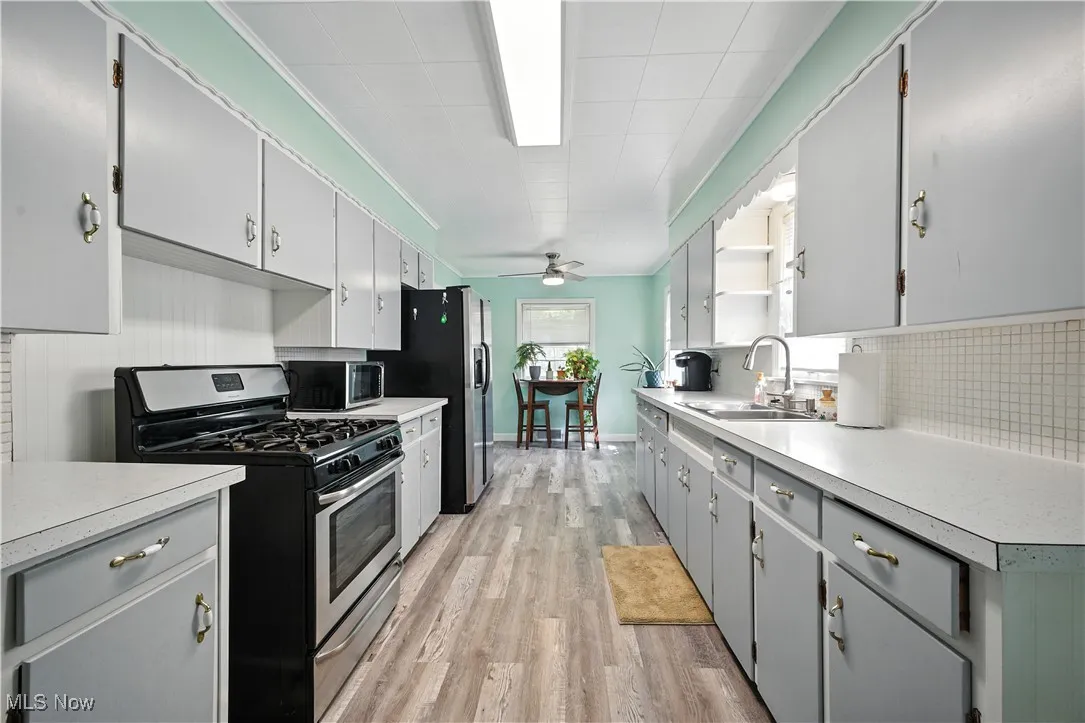 Kitchen with stainless steel appliances, light countertops, light wood-style floors, crown molding, and a ceiling fan