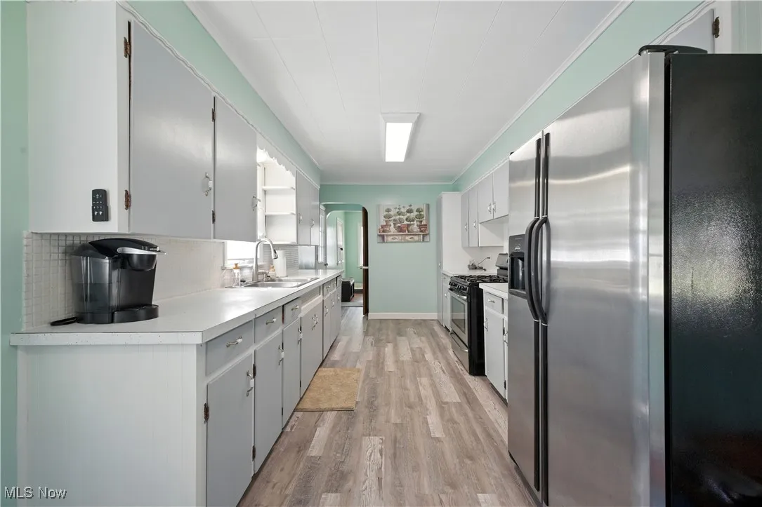 Kitchen with stainless steel appliances, arched walkways, light countertops, light wood-type flooring, and tasteful backsplash