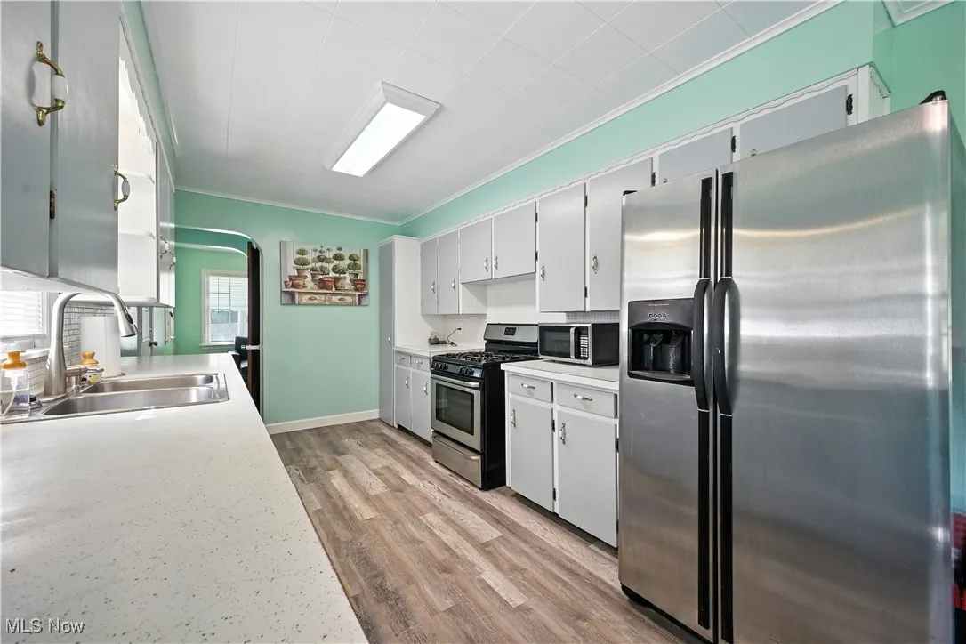 Kitchen featuring stainless steel appliances, light countertops, white cabinets, light wood-style floors, and crown molding