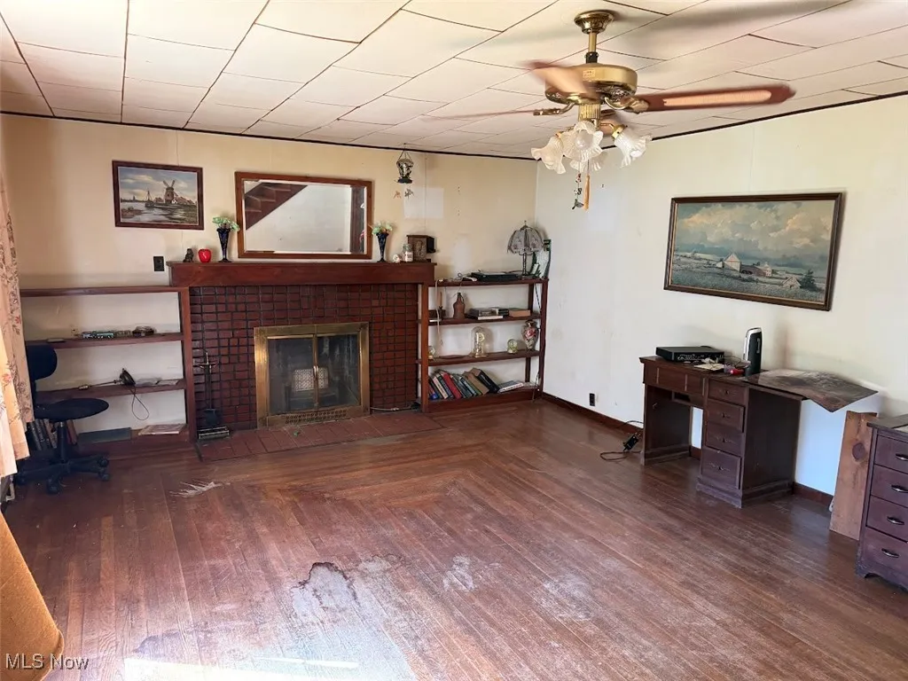 Home office featuring a fireplace, a ceiling fan, and dark wood-style flooring