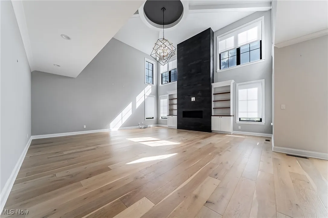 Unfurnished living room featuring light wood-style flooring, a chandelier, and a high ceiling