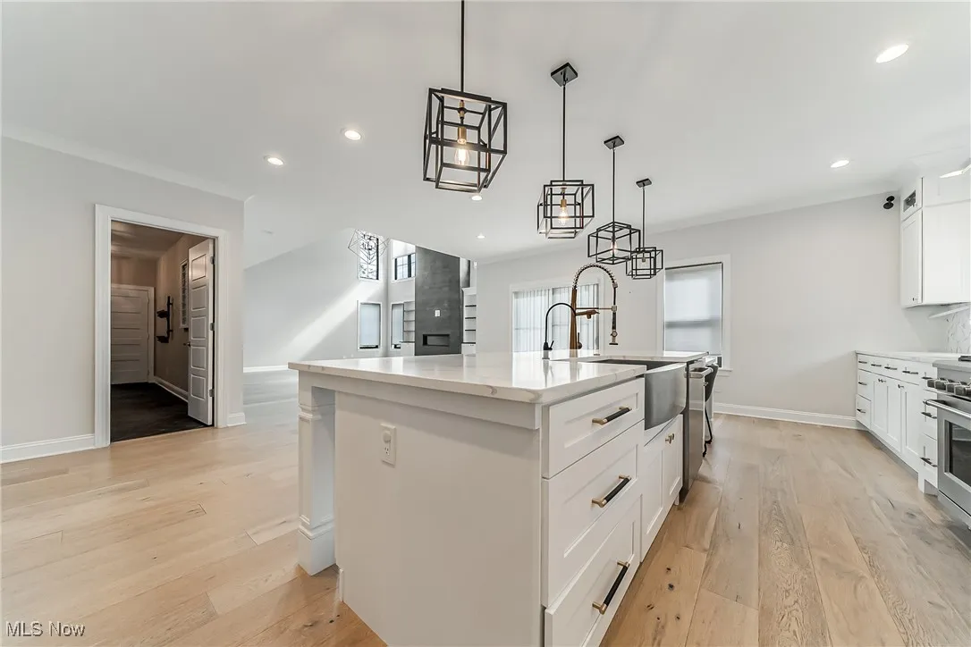 Kitchen with white cabinets, a kitchen island with sink, light wood finished floors, decorative light fixtures, and light stone counters