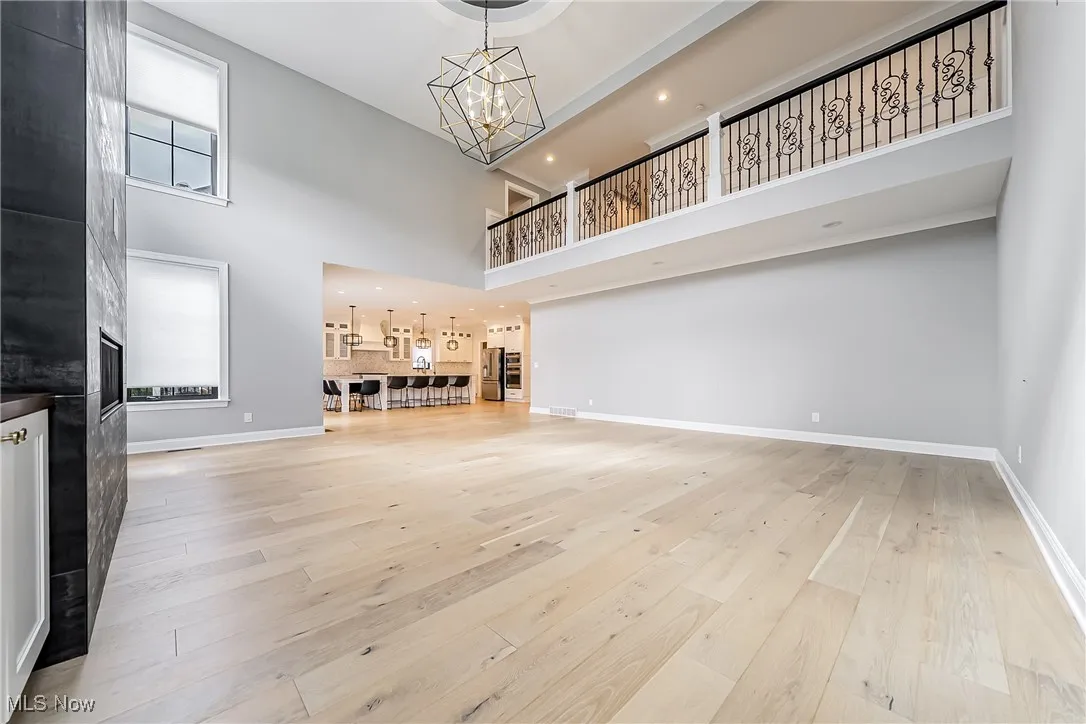 Unfurnished living room with light wood-type flooring, a chandelier, healthy amount of natural light, a towering ceiling, and recessed lighting