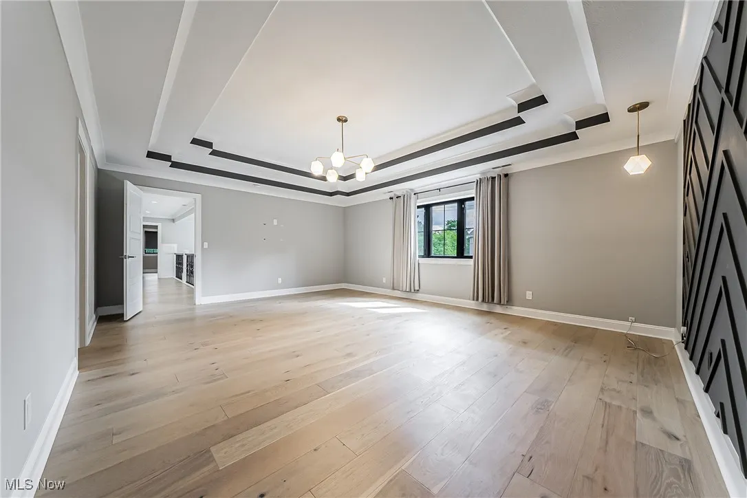 Unfurnished living room featuring a raised ceiling, crown molding, light wood finished floors, and a chandelier