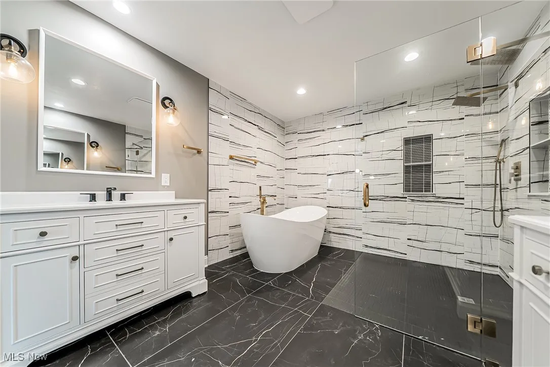 Full bathroom featuring tile walls, vanity, a shower stall, a soaking tub, and dark marble finish flooring