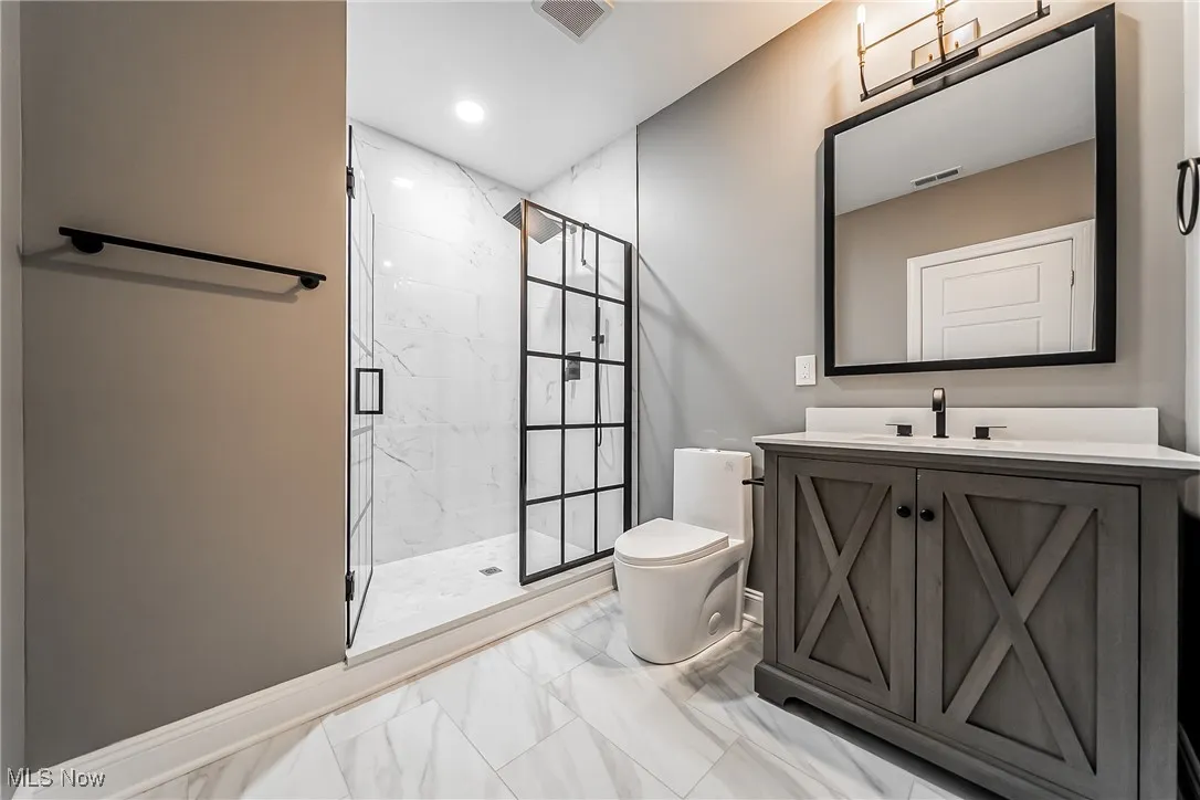 Full bathroom featuring vanity, a marble finish shower, light marble finish floors, and recessed lighting
