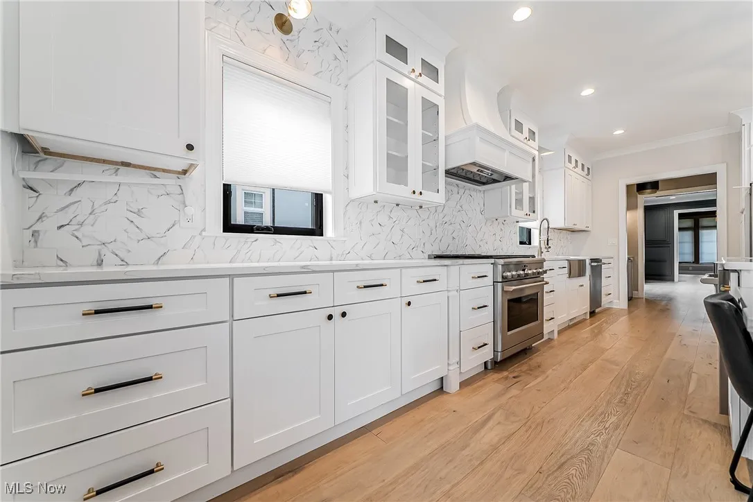 Kitchen with white cabinets, light wood finished floors, high end stainless steel range, recessed lighting, and decorative backsplash