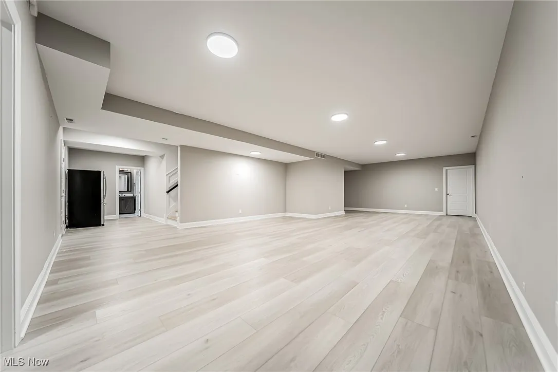 Finished basement with freestanding refrigerator, light wood-type flooring, recessed lighting, and stairs