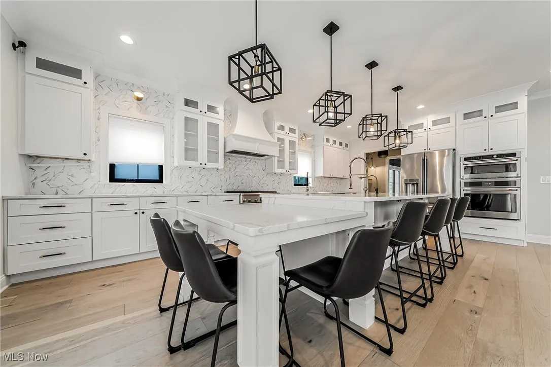 Kitchen with glass insert cabinets, backsplash, white cabinetry, a breakfast bar area, and recessed lighting