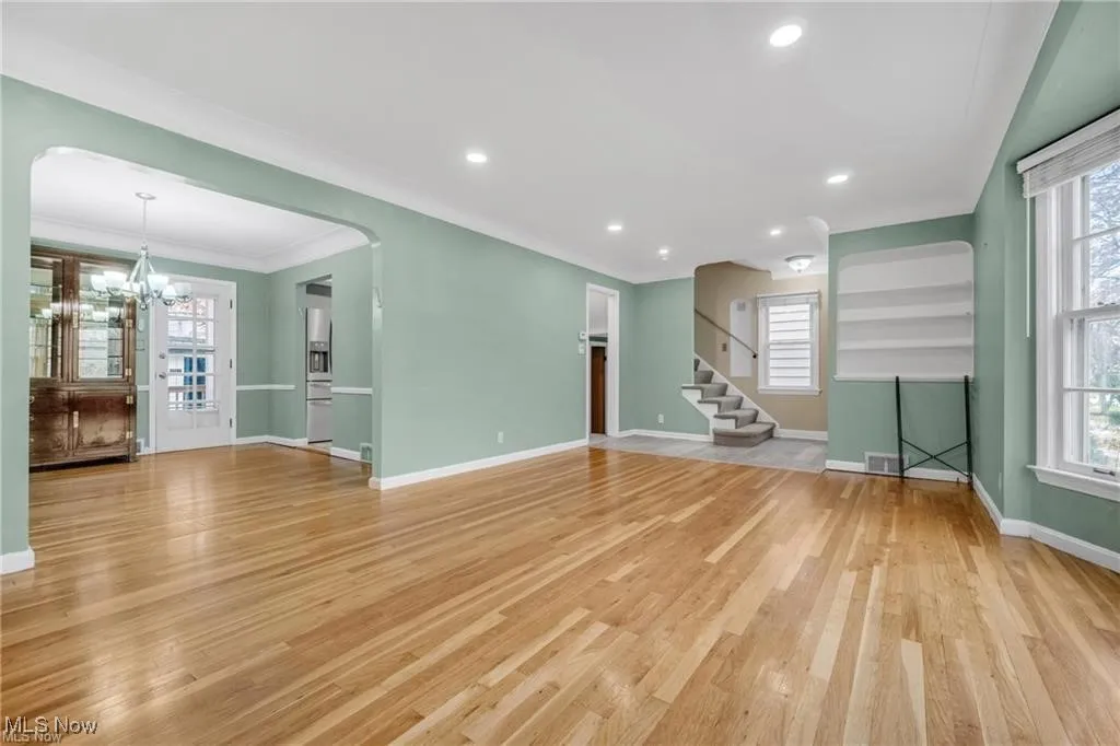 Unfurnished living room featuring light wood-style floors, stairs, recessed lighting, a chandelier, and ornamental molding