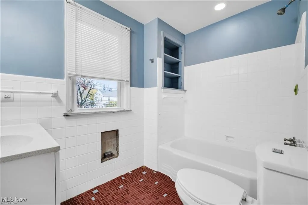 Full bathroom featuring tile walls, vanity, tile patterned floors, wainscoting, and built in shelves