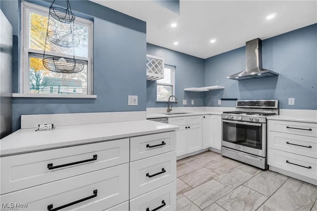 Kitchen featuring gas stove, white cabinetry, wall chimney range hood, recessed lighting, and light stone countertops