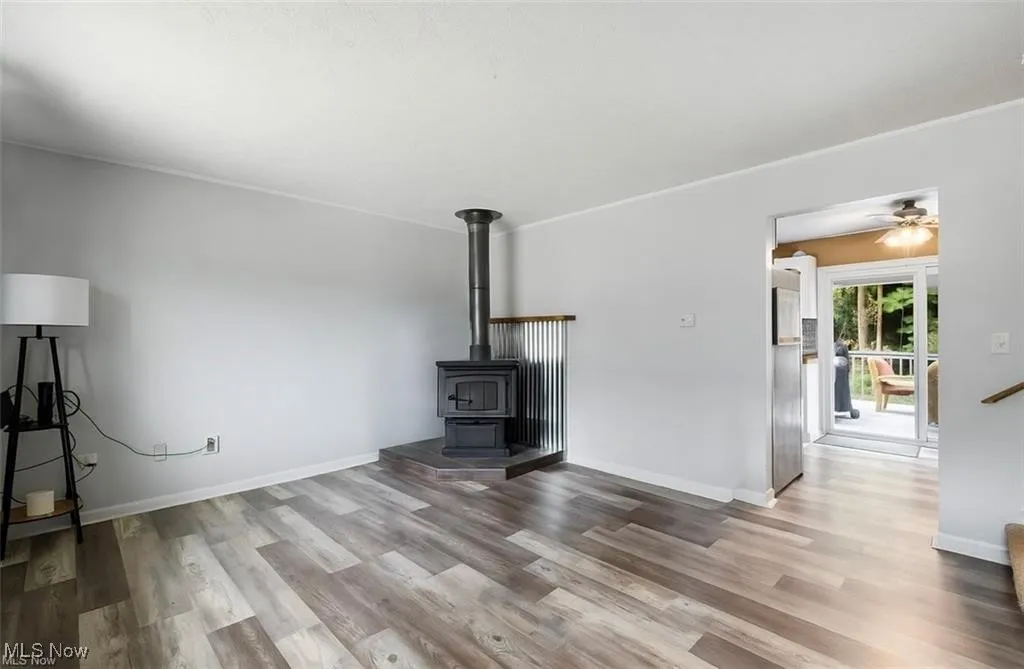 Unfurnished living room with a wood stove, light wood-style floors, and a ceiling fan