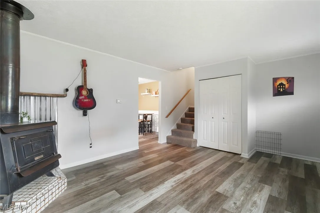 Unfurnished living room with a wood stove, wood finished floors, stairs, and crown molding