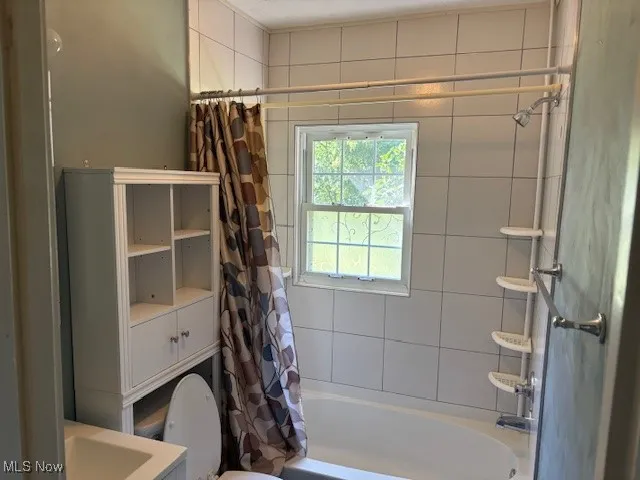 Full bathroom featuring shower / bathtub combination with curtain and toilet
