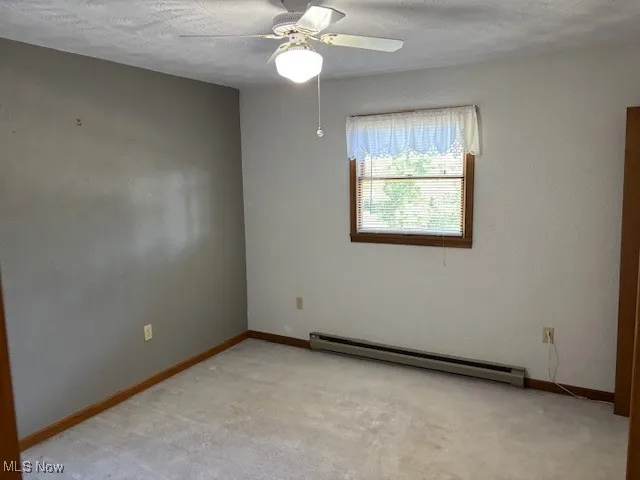 Bedroom featuring baseboard heating, a textured ceiling, a ceiling fan, light carpet, and a textured wall