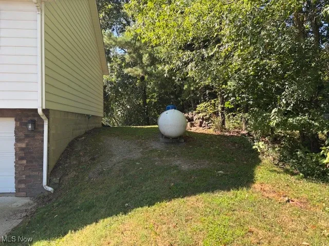 View of grassy yard featuring an attached garage and propane tank