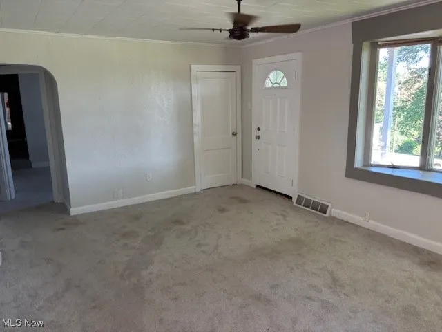 Foyer featuring crown molding, arched walkways, carpet, and a ceiling fan