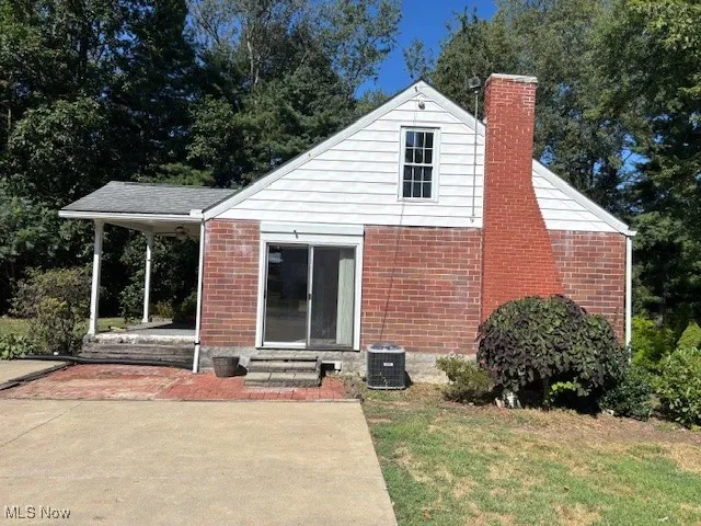 Rear view of house with a chimney, brick siding, a lawn, and entry steps