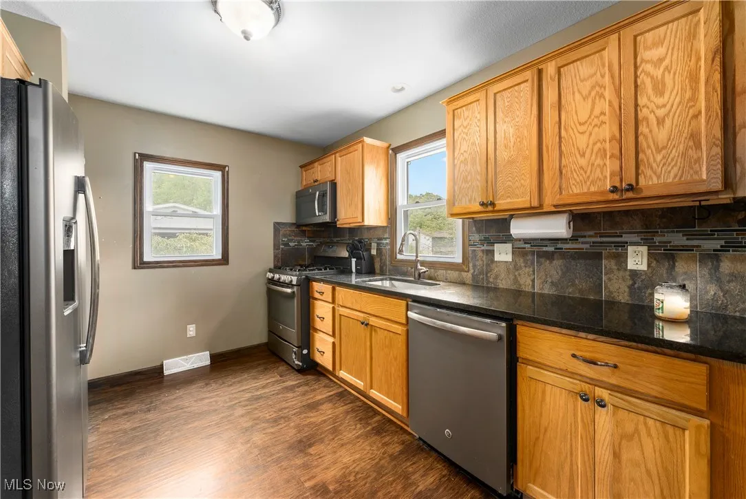 Kitchen with stainless steel appliances, tasteful backsplash, dark wood-style floors, and brown cabinetry