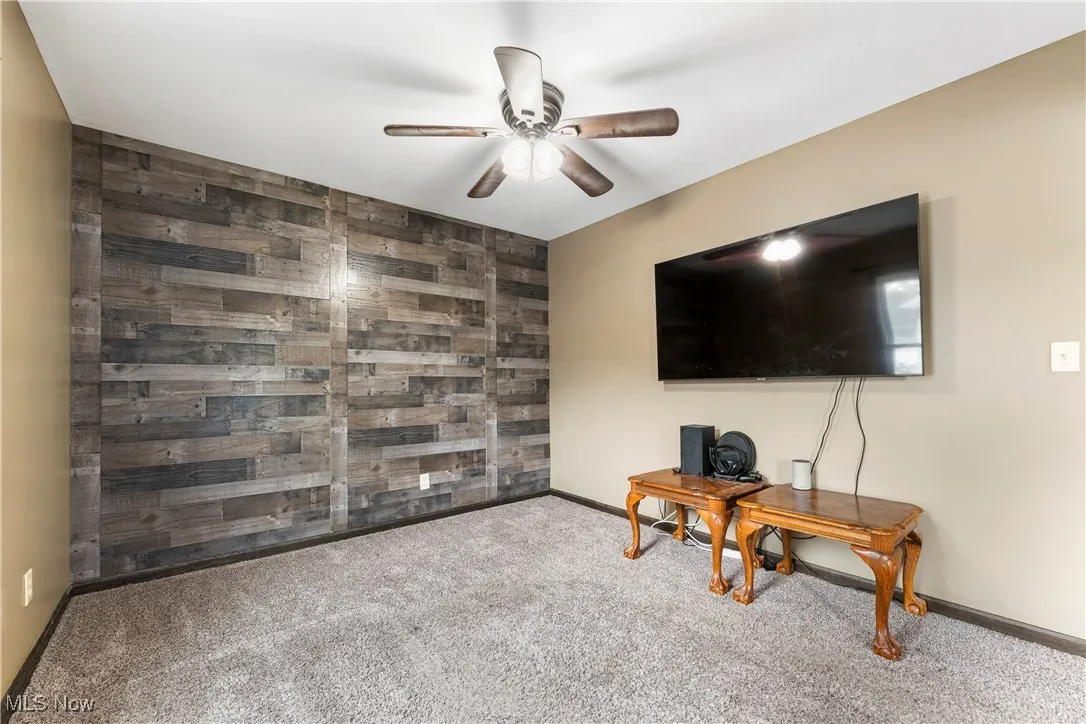 Living area with wood walls, carpet, an accent wall, ceiling fan, and a desk