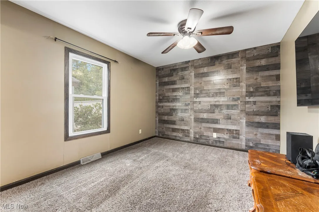 Empty room featuring wooden walls, an accent wall, carpet flooring, and a ceiling fan