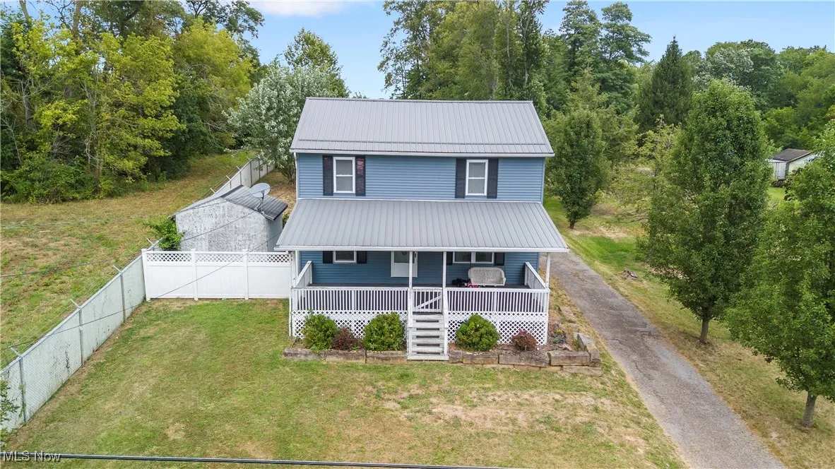 View of front of home with a metal roof, covered porch, a front yard, driveway, and stairs