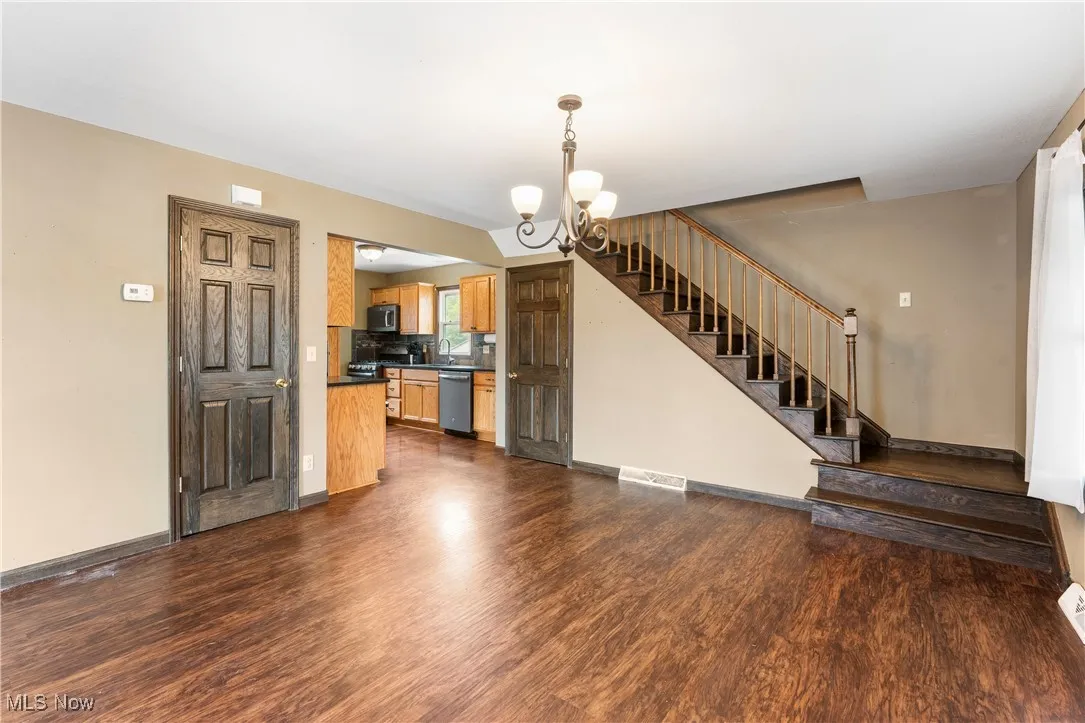 Unfurnished living room with a chandelier, dark wood-style flooring, and stairs