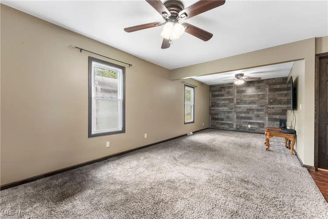 Unfurnished living room featuring wooden walls, carpet flooring, an accent wall, and ceiling fan