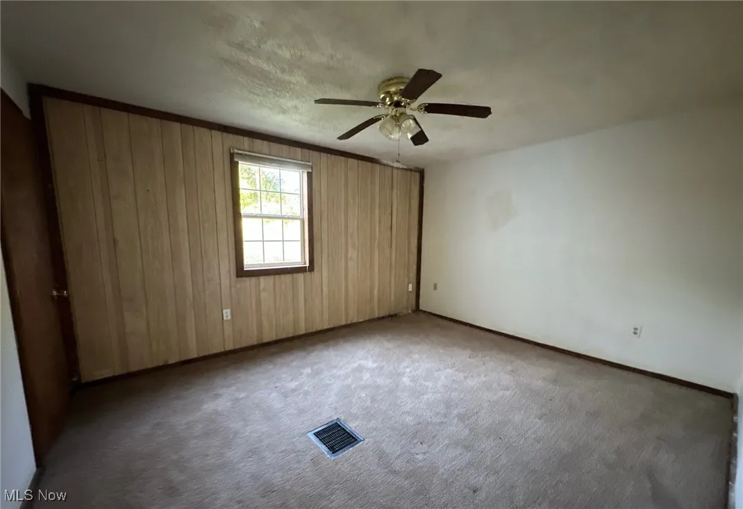 Spare room featuring wood walls, a textured ceiling, carpet flooring, and ceiling fan