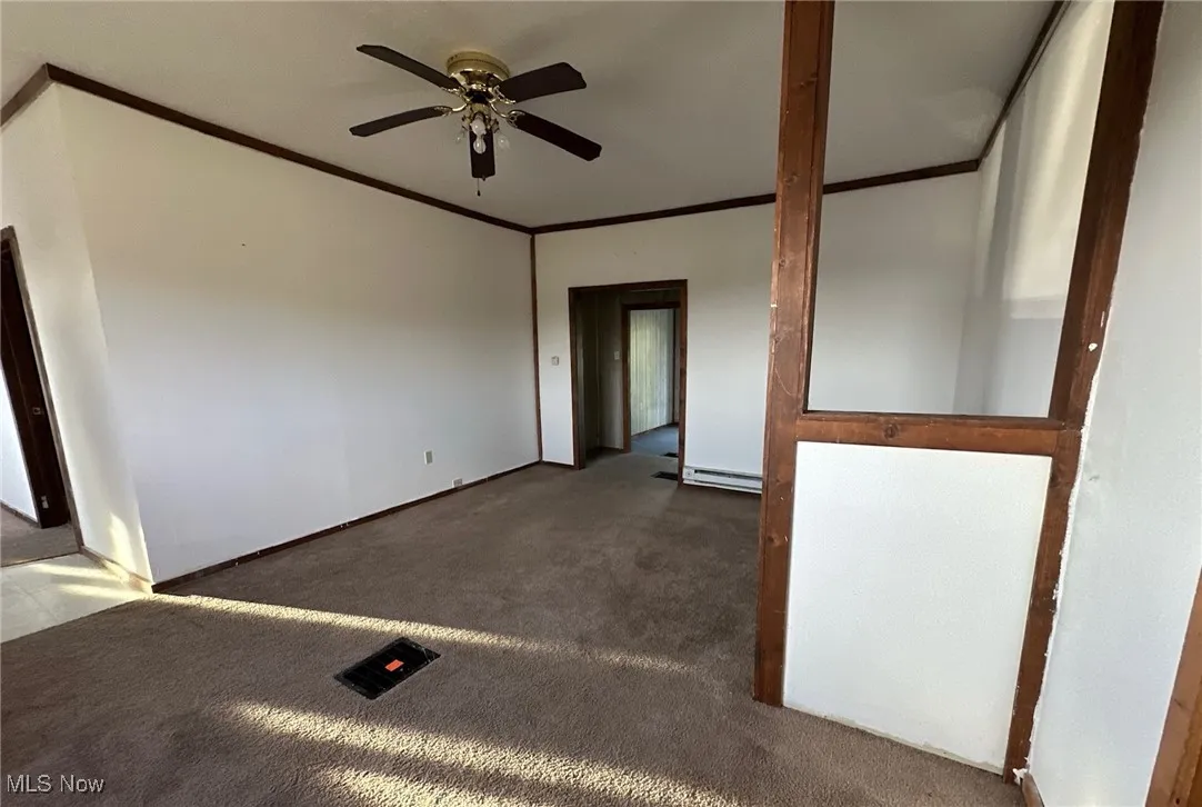 Carpeted empty room with crown molding, ceiling fan, and a baseboard heating unit
