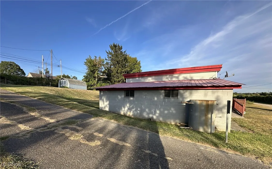 View of property exterior featuring concrete block siding, a storage unit, a metal roof, and a yard