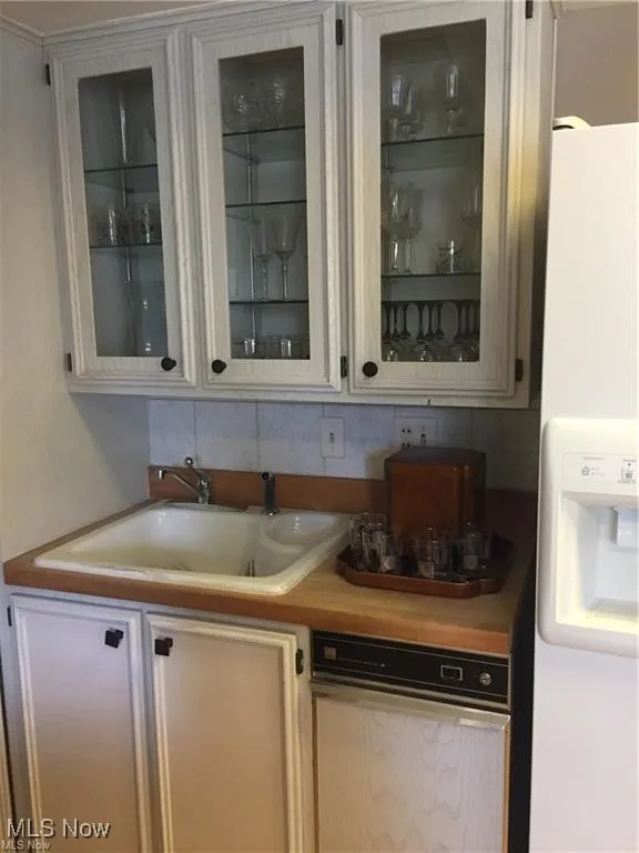 Bar area featuring white fridge with ice dispenser, light countertops, tasteful backsplash, and white cabinetry