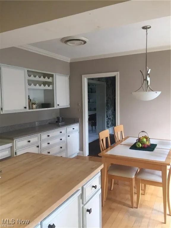 Kitchen featuring white cabinetry, wood counters, crown molding, pendant lighting, and light wood finished floors