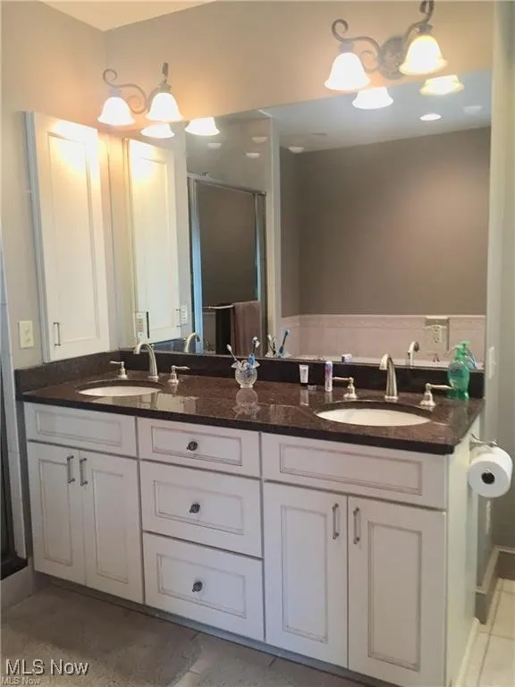 Bathroom with double vanity, light tile patterned floors, and a stall shower