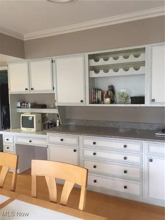 Kitchen featuring white cabinets, ornamental molding, light wood-type flooring, open shelves, and light stone countertops