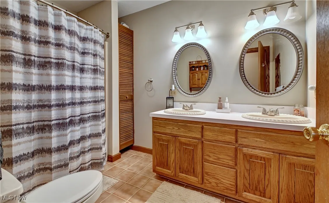 Full bathroom featuring light tile patterned floors, double vanity, and curtained shower